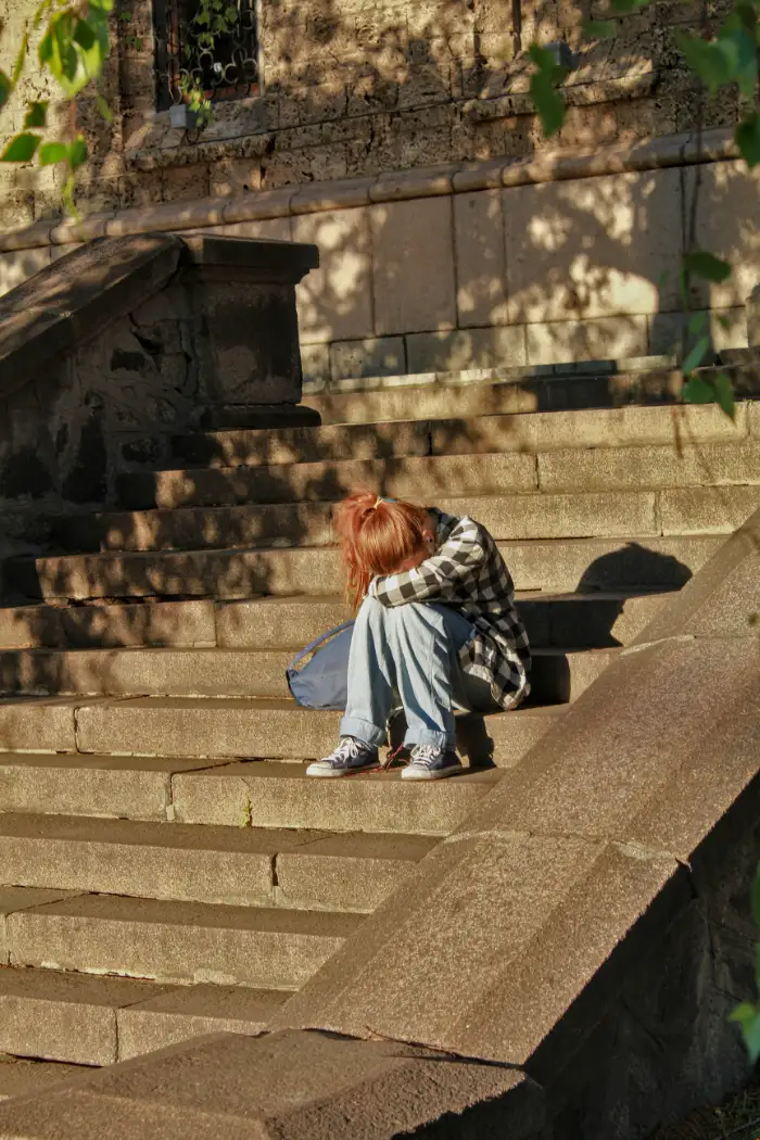 Jugendliche Person sitzt allein und zusammengesunken auf einer Treppe, Kopf auf die Knie gelegt, symbolisiert Ausgrenzung und Mobbing im Alltag