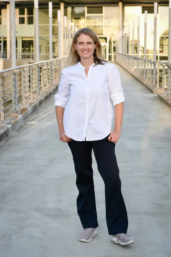 Nicole Tepaße von Rede Klartext steht auf einer Brücke vor einem modernen Gebäude und präsentiert sich als Deeskalationstrainerin