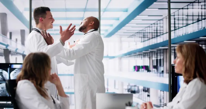 Medizinisches Team in Weißkitteln diskutiert lebhaft im Klinikflur, symbolisiert angespannte Situation vor einem Deeskalationstraining für Fachkräfte